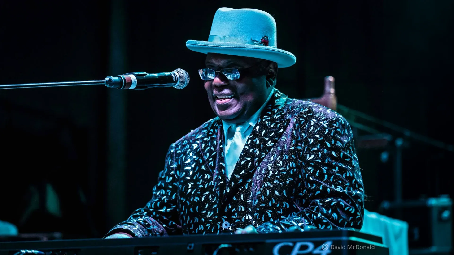 Kenny “Blues Boss” Wayne con cappello e occhiali canta al microfono dietro la tastiera - Teatro Massimo di Cagliari - 3 ottobre 2026